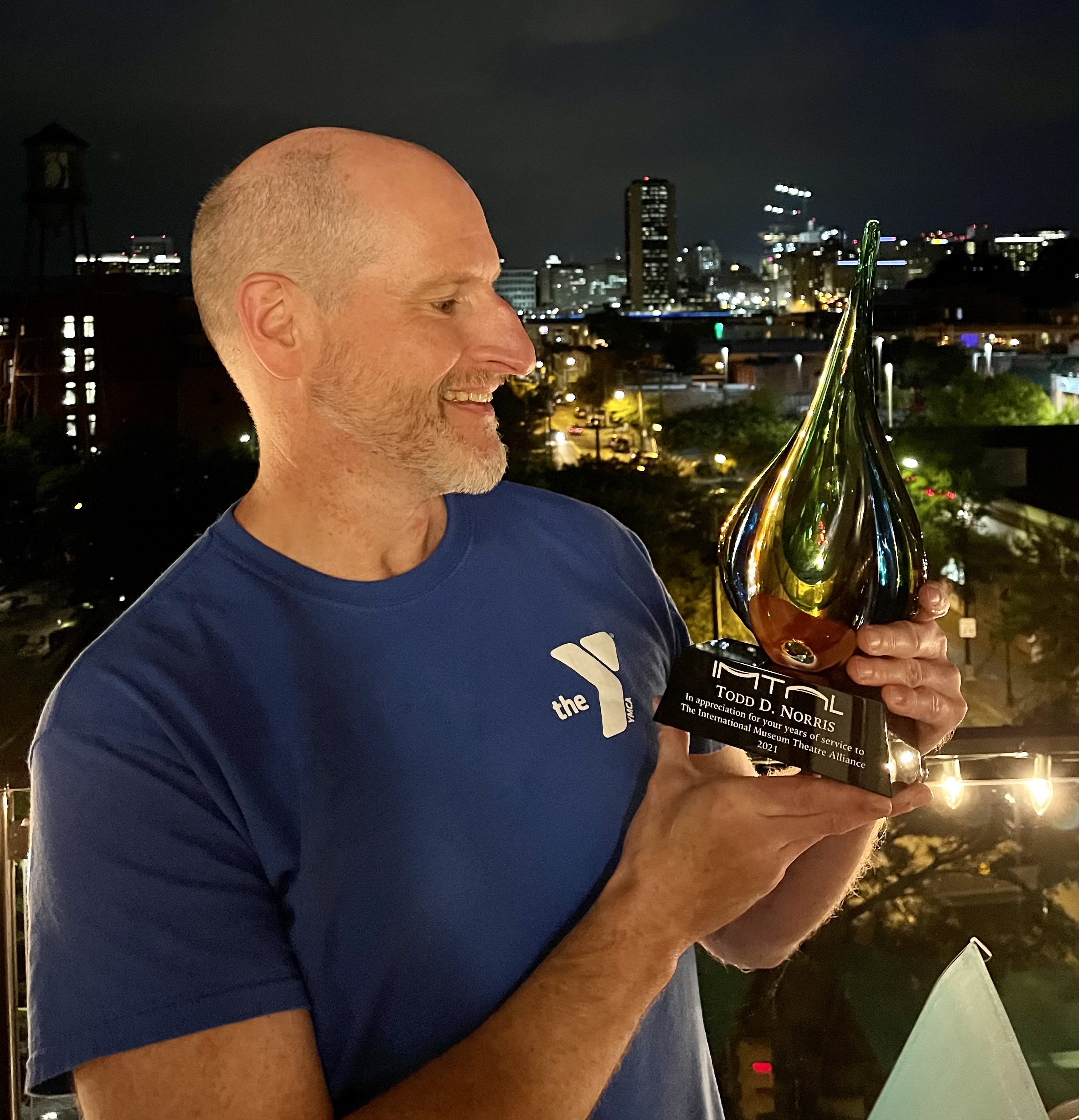 photo is Todd D. Norris holding a glass recognition award. He is standing on a balcony overlooking the city of Richmond, VA at night.